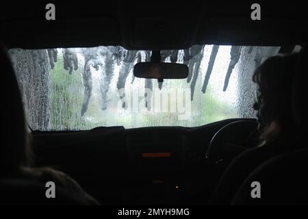 Blick aus dem Inneren eines Autos, während es durch eine automatische Waschanlage fährt, nasse Windschutzscheibe. Stockfoto