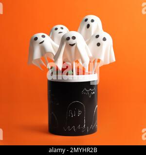 Köstlicher, geisterförmiger Kuchen auf orangefarbenem Hintergrund. Halloween-Feier Stockfoto