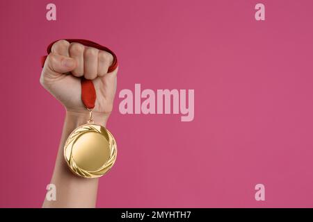 Frau mit Goldmedaille auf pinkfarbenem Hintergrund, Nahaufnahme. Raum für Design Stockfoto