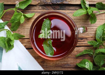 Tasse mit heißem aromatischem Pfefferminztee und frischen Blättern auf einem Holztisch, flach liegend Stockfoto