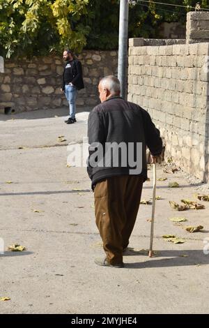 Ein älterer Mann läuft mit einem Stock die Straße runter in seinem Dorf im Nordirak Stockfoto