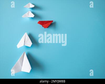 Rotes Papierflugzeug Origami verlässt andere weiße Flugzeuge auf blauem Hintergrund. Konzept der Führungsqualitäten. Stockfoto