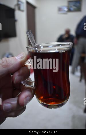Eine weiße Hand, die eine Tasse starken schwarzen Tee in einer türkischen Teetasse hält. Stockfoto