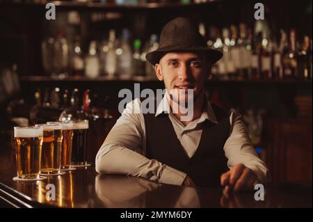 Fröhlicher Barkeeper an der Bar mit Gläsern Bier im Pub Stockfoto