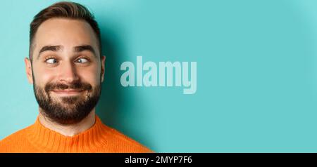 Kopfbild des lustigen kaukasischen Mannes, der Gesichter macht, schielend und lächelnd dumm, über hellblauem Hintergrund stehend Stockfoto