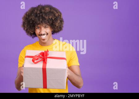 Glücklicher afrikaner, der vor der Kamera lächelt, während er ein Geschenk überreicht Stockfoto