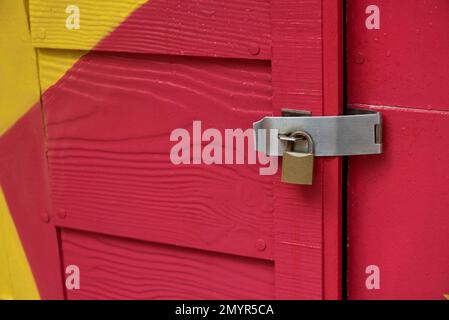 Verriegeltes Vorhängeschloss mit Kette an farbenfroher Holztür. Stockfoto