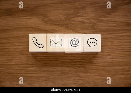 Verschiedene Kontaktansätze. Symbol für Telefon, E-Mail, Post und Chat auf einem hölzernen Würfel. Stockfoto