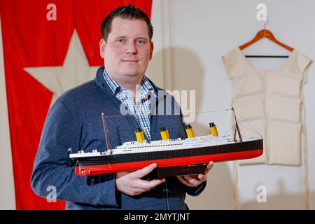 Flintbek, Deutschland. 21. Januar 2023. Malte Fiebing-Petersen, Vorsitzender des Deutschen Titanic-Verbandes, hält ein Modell der Titanic, während er vor einem Banner der White Star Line-Schifffahrtsgesellschaft und einer Schwimmweste steht, die beide als originale Requisiten im Film verwendet wurden. Der Film Titanic wurde vor 25 Jahren am 08. Februar 1998 vorgestellt. Kredit: Axel Heimken/dpa/Alamy Live News Stockfoto