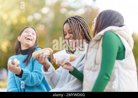 Freunde genießen den Park, während sie Hot Dogs essen Stockfoto