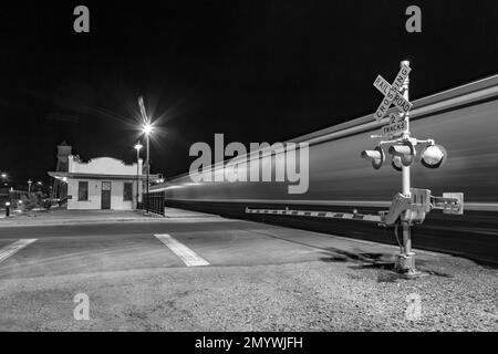 Der Zug fährt nachts am Bahnübergang vorbei. Der Bahnhof Kingman der Santa Fee Railroad wurde 1907 eröffnet und ist noch in Betrieb. Stockfoto