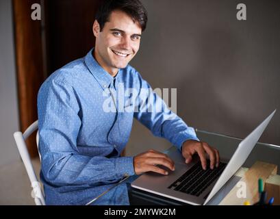 Er ist ein Draufgänger. Porträt eines selbstbewussten jungen Geschäftsmanns, der mit einem Laptop an seinem Schreibtisch sitzt. Stockfoto
