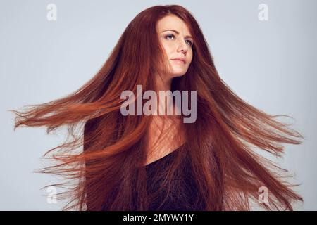 Flammende Haarschönheit. Studioaufnahme einer jungen Frau mit wunderschönen roten Haaren, die vor grauem Hintergrund posiert. Stockfoto