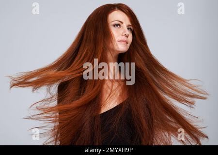 Flammende Haarschönheit. Studioaufnahme einer jungen Frau mit wunderschönen roten Haaren, die vor grauem Hintergrund posiert. Stockfoto