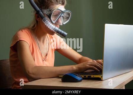 Ein ukrainisches Mädchen sitzt in einer Taucherbrille und Handsets an einem Laptop auf einem Tisch zu Hause und träumt vom Urlaub Stockfoto