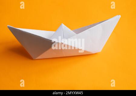 Weißes Papierboot auf orangefarbenem Hintergrund Stockfoto