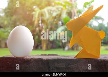 Farbenfrohe und süße Hasenpappe Origami mit Ei im Garten. Happy Easter Celebration Konzept. Stockfoto