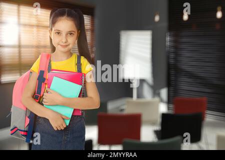 Kleines Mädchen mit Schulpapier in leerem Klassenzimmer Stockfoto