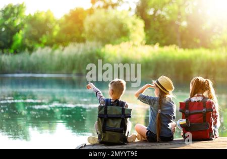 Schulferien. Gruppe von Kindern, die auf einem hölzernen Pier in der Nähe des Flusses sitzen Stockfoto