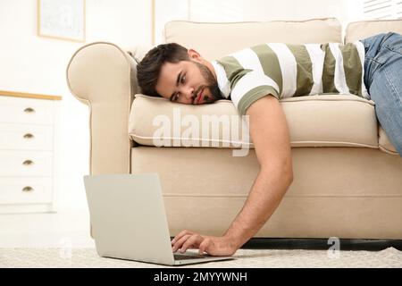 Fauler junger Mann, der zu Hause auf dem Sofa auf dem Laptop liegt Stockfoto