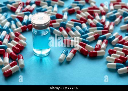 Eine Flasche Impfstoff neben anderen Medikamenten-Pillen oder Kapseln auf blauem Hintergrund. Stockfoto