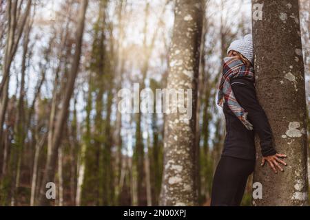 Eine Frau lehnt sich in einem wunderschönen Wald gegen den Stamm eines Baumes. Sie umarmt den Baum und spürt ihn. Begriff des Naturkontakts und Balneothe Stockfoto