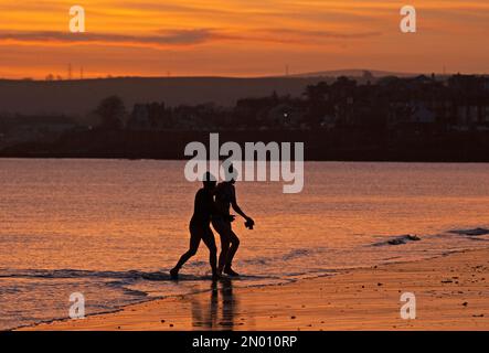 Portobello, Edinburgh, Schottland, Vereinigtes Königreich, 5. Februar 2023. Kühler, farbenfroher Himmel bei Sonnenaufgang über dem Firth of Forth und dem Strand am Meer für die wenigen Menschen, die ihn erleben. Temperatur 1 Grad Celsius mit Eis auf nassen Oberflächen und Autoscheiben. Abbildung: Zwei Schwimmer mit kaltem Wasser im Firth of Forth für ein kühles Bad. Kredit: Archwhite Stockfoto