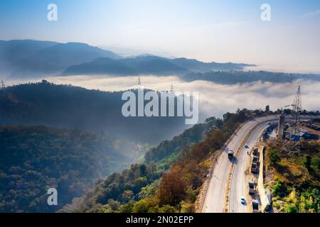 Die Drohne aus der Luft wurde vom Mountain Hill Road Highway aufgenommen, wobei Autos auf dem Highway in ein Tal mit Nebel-Wolken fahren, die sich bis in die Ferne erstrecken Stockfoto