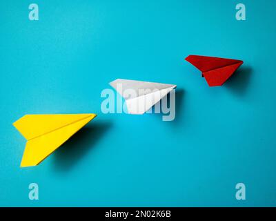 Rotes Papierflugzeug Origami führende weiße und gelbe Flugzeuge auf blauem Hintergrund mit anpassbarem Platz für Text. Konzept der Führungsqualitäten Stockfoto