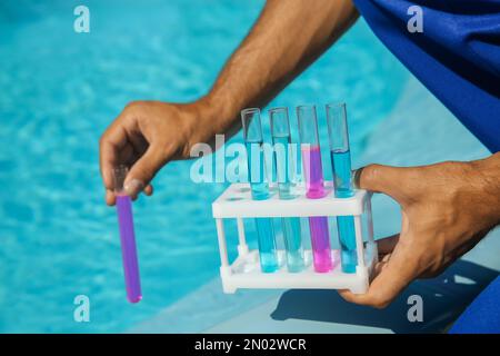 Mann hält Reagenzgläser mit Reagenzien in der Nähe des Schwimmbeckens, Nahaufnahme Stockfoto