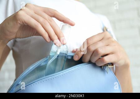 Frau, die Handdesinfektionsmittel in Handtasche steckt, auf hellem Hintergrund, Nahaufnahme. Persönliche Hygiene während der COVID-19-Pandemie Stockfoto