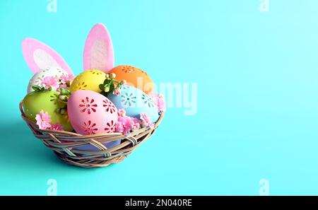 Bunte Ostereier im Korb mit Hasenohren und Blumen auf blauem Hintergrund. Pastellfarbene Ostereier Stockfoto