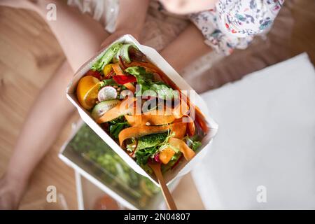 Papierbehälter, Lebensmittelzustellungskonzept. Das Mädchen isst einen grünen Salat aus Brokkoli, grünen Bohnen, Gurke und Avocado. Gesunde Ernährung. Draufsicht, Kopierbereich Stockfoto