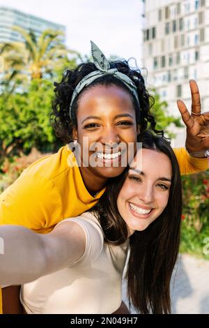 Zwei multiethnische weibliche Freunde, die sich mit dem Mobiltelefon im Freien fotografieren Stockfoto