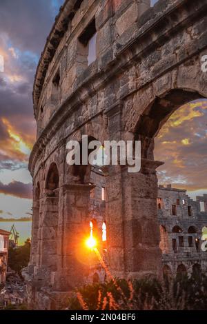 Sonnenuntergang über dem Himmel mit Pula Arena. Römisches Amphitheater zur Goldenen Stunde in Kroatien. Außenansicht eines vertikalen Wahrzeichens am Abend in Istrien. Stockfoto