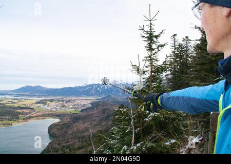 Füssen, Deutschland - Januar 14. 2023: Ein Reiseleiter erläutert das Panorama mit seinen Wanderstöcken Stockfoto