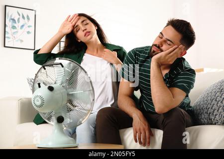 Ein Paar, das zu Hause vor dem Ventilator an Hitze leidet. Sommersaison Stockfoto