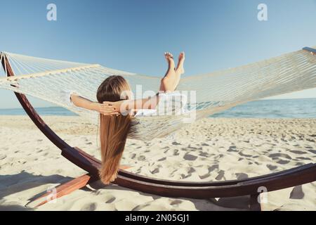 Junge Frau, die sich in einer Hängematte am Strand entspannt Stockfoto