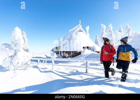 Mutter und Sohn auf einem Winterausflug mit der Familie nach Velika planina, Alpenwiesen in den slowenischen alpen, entspannen in der idyllischen traditionellen Holzhütte Stockfoto