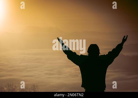 Mann betet bei Sonnenuntergang Berge erhöhte Hände Reisen Lifestyle spirituelle Entspannung emotionales Konzept, Freiheit und Reiseabenteuer. Stockfoto