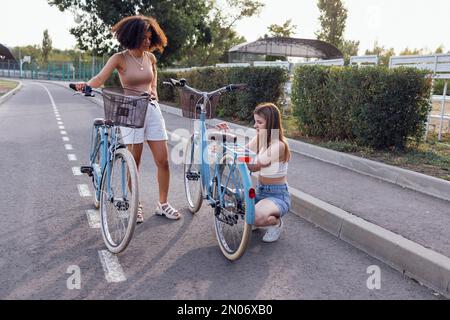 Teenager verschiedener Nationalitäten und Aussehen auf Fahrrädern fahren entlang einer Straße der Stadt. Junge und positive Mädchen lächeln zusammen und reparieren Fahrräder. Er Stockfoto