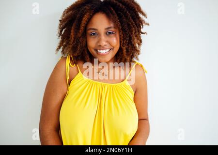 Wunderschöne, kurvige, übergroße junge afto-amerikanische Frau in einem gelben Kleid zu Hause. Körperpositive, stilvolle, lächelnde Frau hat eine entspannte Zeit. Karosserieabnahme an Stockfoto