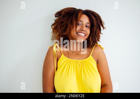 Wunderschöne, kurvige, übergroße junge afto-amerikanische Frau in einem gelben Kleid zu Hause. Körperpositive, stilvolle, lächelnde Frau hat eine entspannte Zeit. Karosserieabnahme an Stockfoto