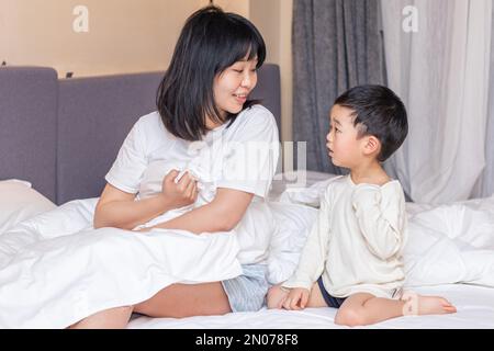 Die Mutter deckte die Decke auf dem Bett, um zu spielen Stockfoto