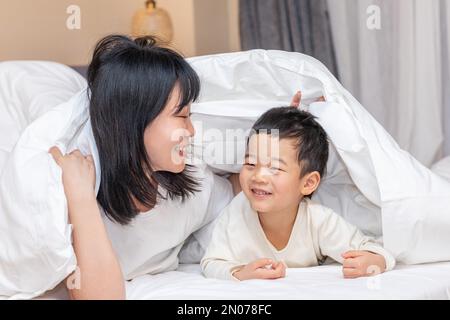 Die Mutter deckte die Decke auf dem Bett, um zu spielen Stockfoto