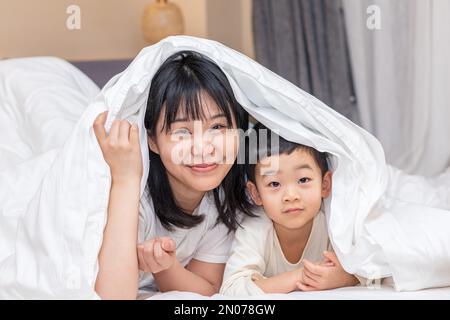 Die Mutter deckte die Decke auf dem Bett, um zu spielen Stockfoto