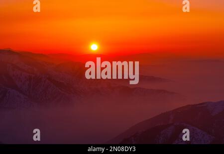 Magische Atmosphäre eines Sonnenuntergangs am Abend im Hochland; Bergketten und Täler umgeben von sanftem Nebel bei Sonnenuntergang Stockfoto