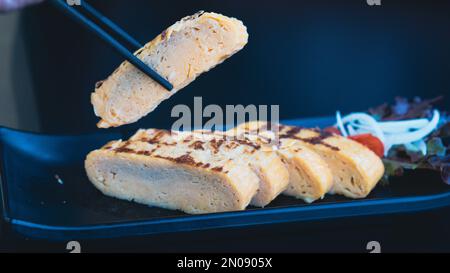 Stäbchen halten Tamagoyaki, weiches, süßes Omelett auf Japanisch Stockfoto