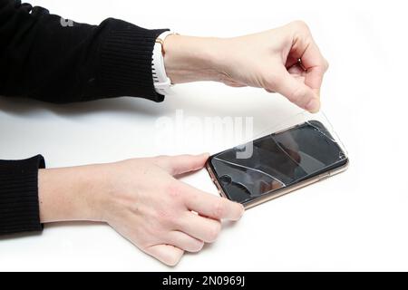 Das Detail, wie die Hände das zerbrochene Schutzglas mit Rissen vom Smartphone-Touchscreen entfernen. Stockfoto