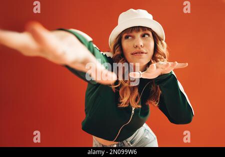 Lebendige weibliche Hipster tanzen und Spaß in einem Studio haben. Eine stilvolle junge Frau, die ein paar Bewegungen macht, während sie auf einem orangefarbenen Hintergrund steht Stockfoto